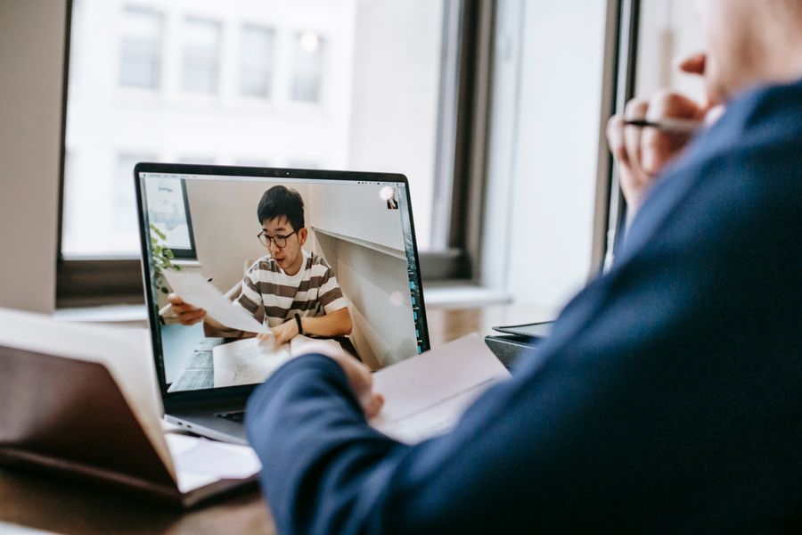 A tutor on a laptop screen holding up a worksheet during an online class