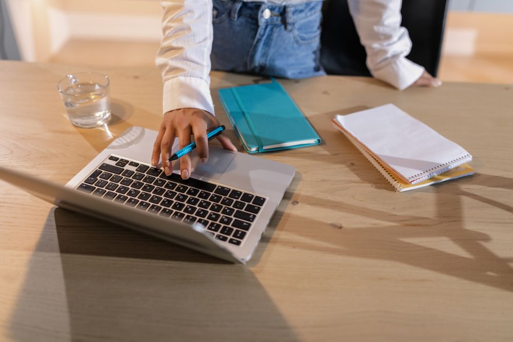 A laptop and notebooks on a wooden desk, seen from above