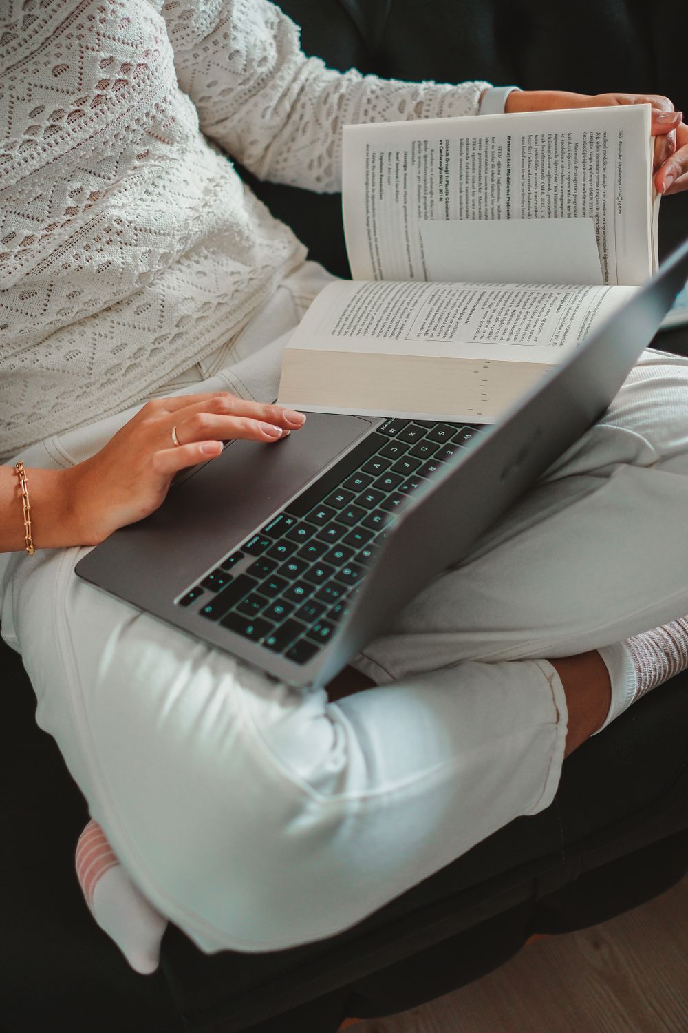 A woman sitting cross-legged with a laptop and a book